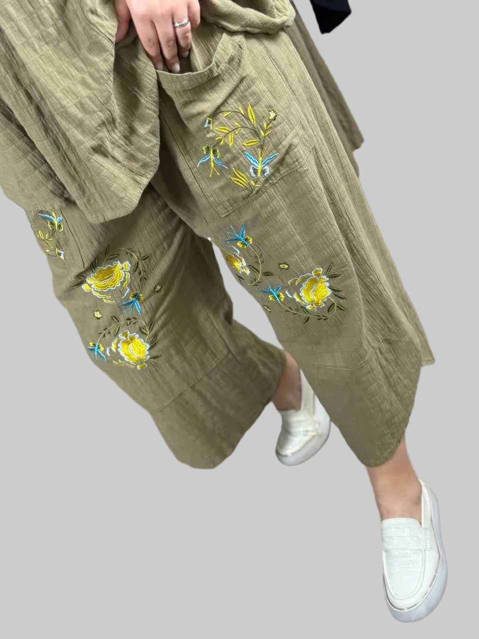 Green embroidered pants worn by a person on a wooden floor.
