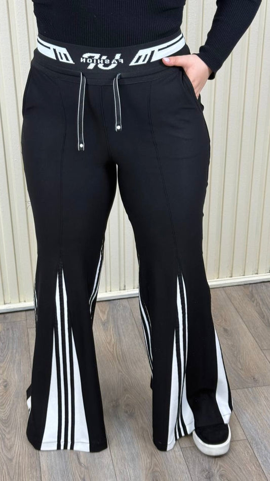 Black pants with white stripes and a brand logo worn by a person against a neutral background