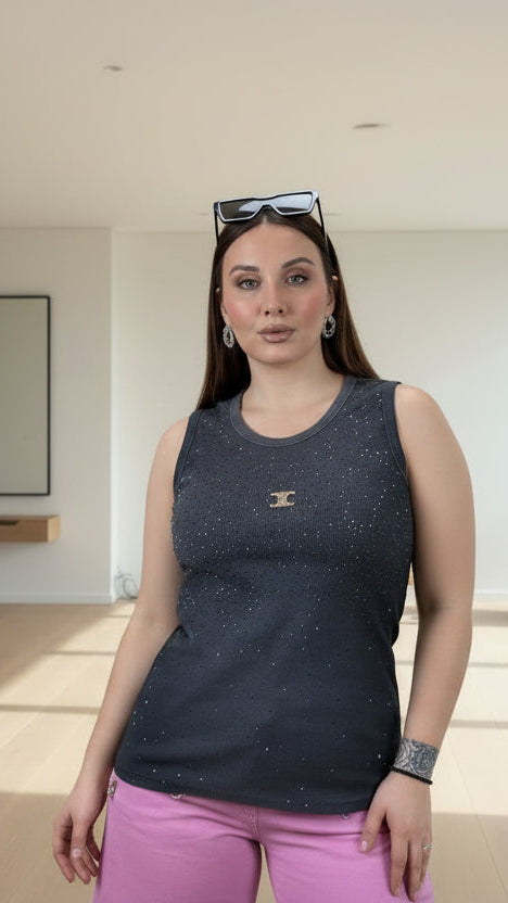 Woman taking a mirror selfie wearing a dark blue sleeveless top with white speckles and pink pants, with a decorative wall in the background.