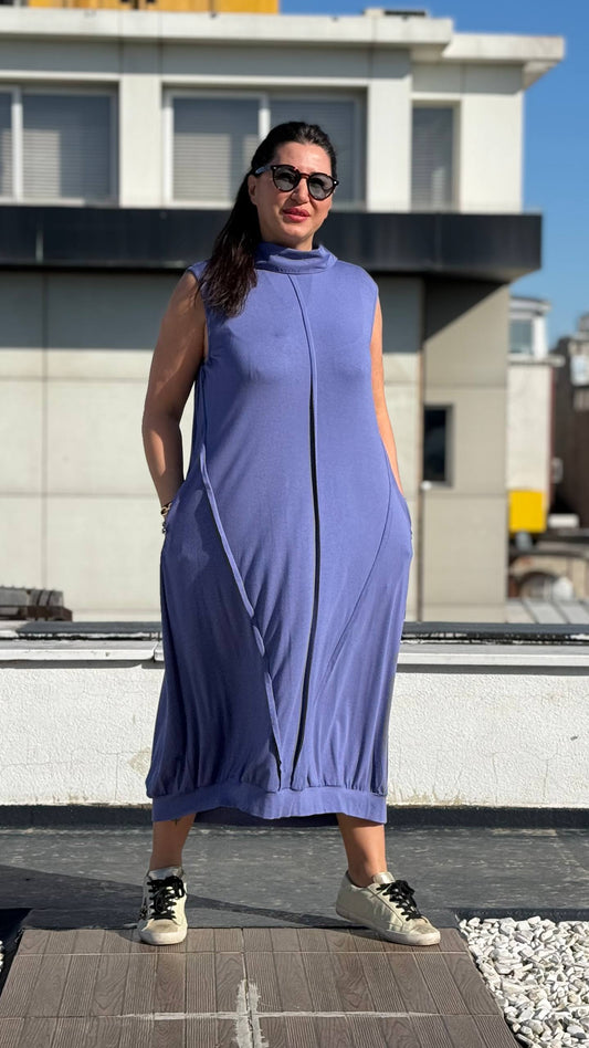 Woman in a blue dress standing on a rooftop with buildings in the background