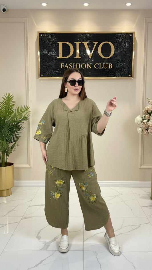 Woman taking a mirror selfie wearing an olive green outfit with floral embroidery in a clothing store.