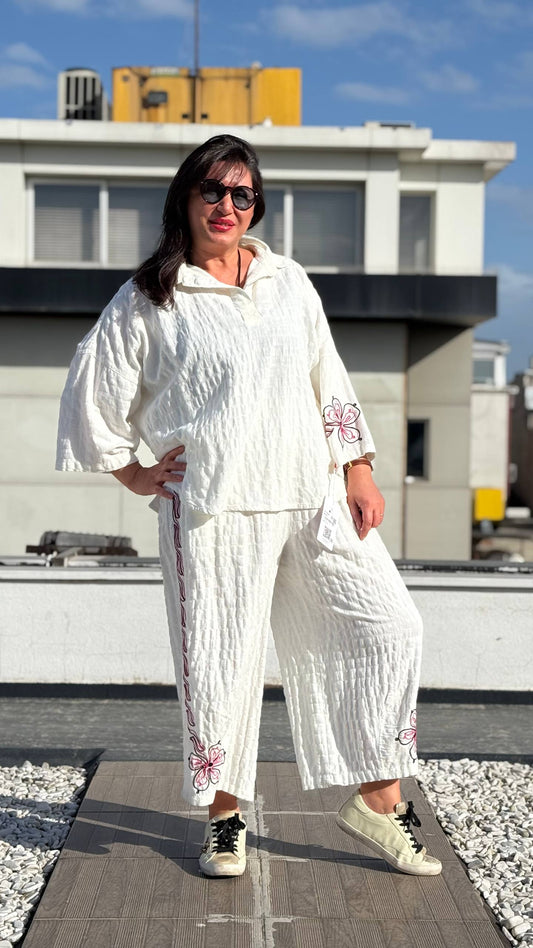 Woman in a white outfit with floral patterns standing on a rooftop.